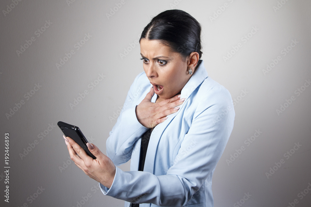 Young corporate business woman shocked with a message she receives on her cell phone Young corporate business woman shocked with a message she receives on her cell phone