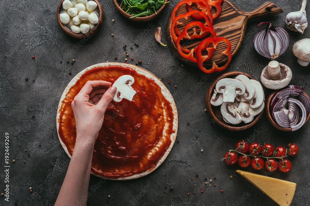 Φωτογραφία cropped shot of woman putting mushroom slice onto pizza dough onto pizza on conc