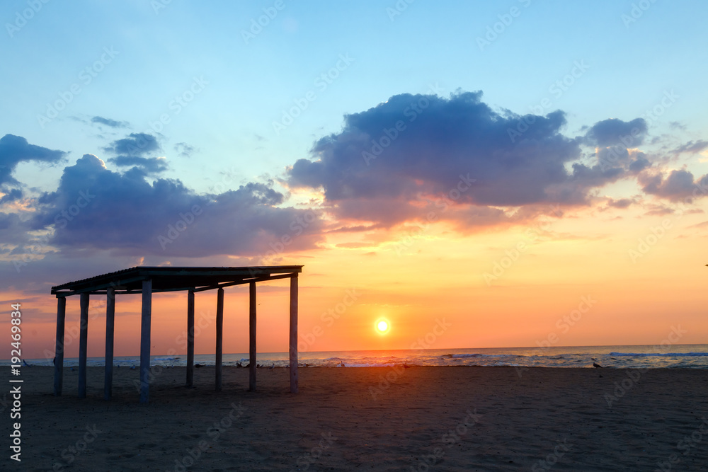 Silhouette gazebo on an empty sandy beach at sunset.