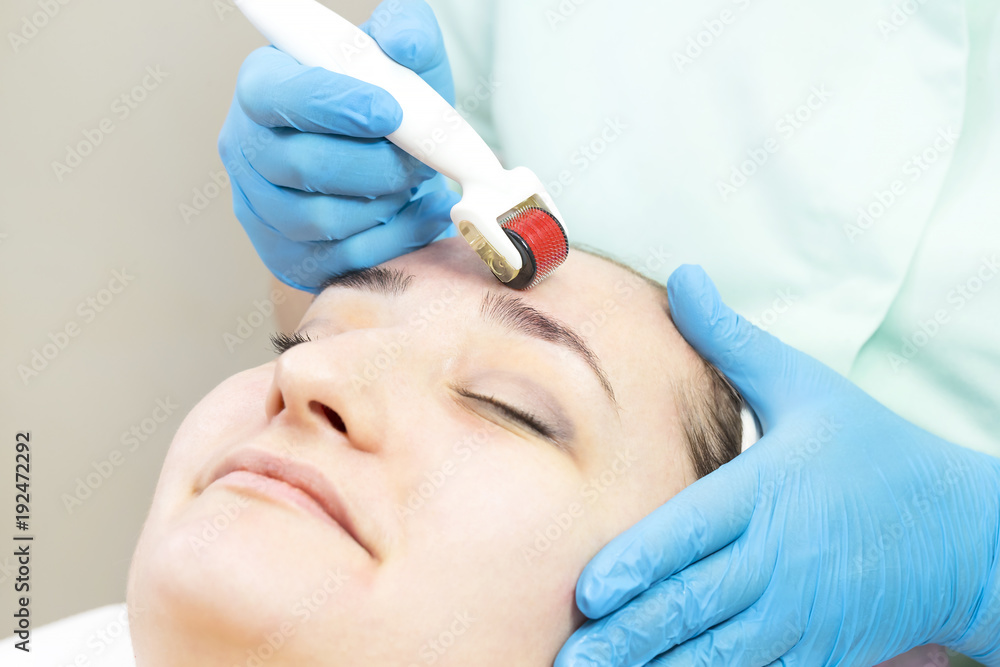 The woman undergoes the procedure of medical micro needle therapy with a modern medical instrument derma roller 