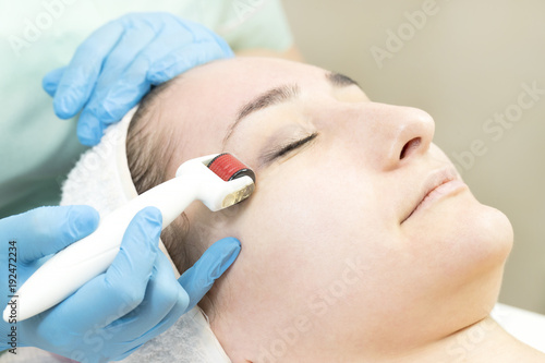 The woman undergoes the procedure of medical micro needle therapy with a modern medical instrument derma roller 