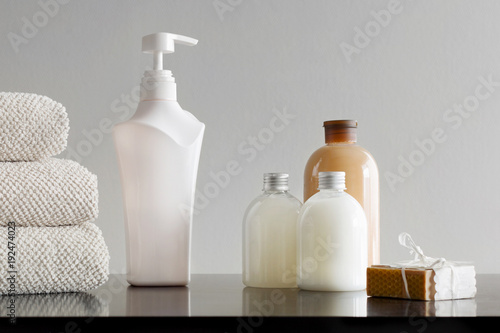 Stack of towels with shampoo, body lotion, shower milk and handmade soap. Neutral background.