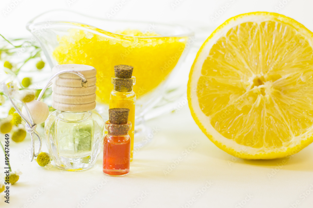 Fruit aromatherapy concept with essential oil in glass bottles, a bowl of bath sea salt, flowers and lemon, white background, close up Fruit aromatherapy concept with essential oil in glass bottles, a bowl of bath sea salt, flowers and lemon, white background, close up