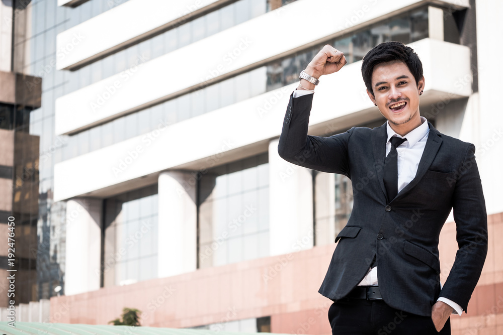 Portrait of young Asian businessman in black suit standing with office building background. Free space for text Portrait of young Asian businessman in black suit standing with office building background. Free space for text