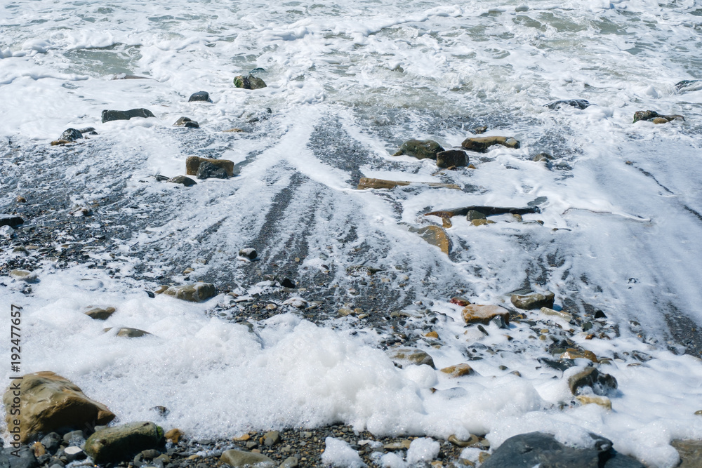 Sea wave rolls down from the stone shore, leaving the foam on the beach.