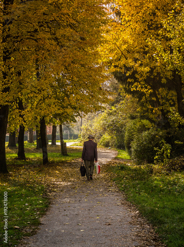 Old man walking with bags through the park in autumn