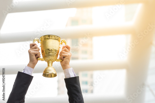 hand of a businessman happy expression holding a golden trophy his success. Make winner gesture