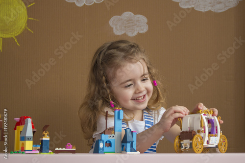 Cute funny preschooler little girl playing with construction toy blocks in kindergarten room. background painted by the sun and clouds