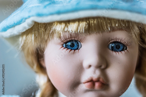 Close-up of beautiful porcelain doll with blond hair and blue eyes, sky blue vintage dress and leather shoes. Little princess games.