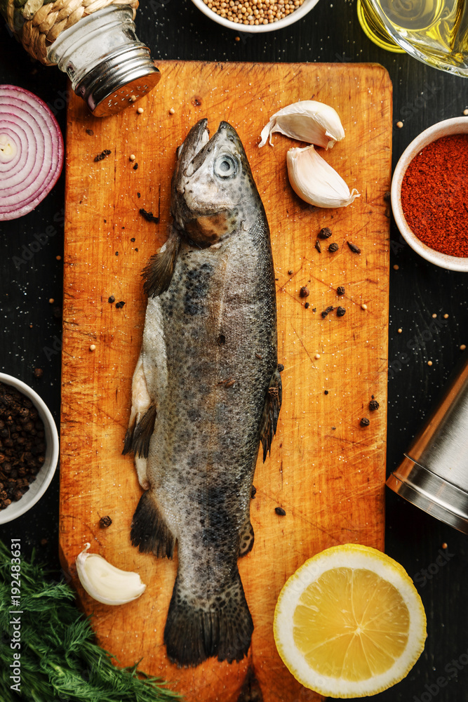 Fresh fish with herbs and spices on vintage cutting board on dark background, top view