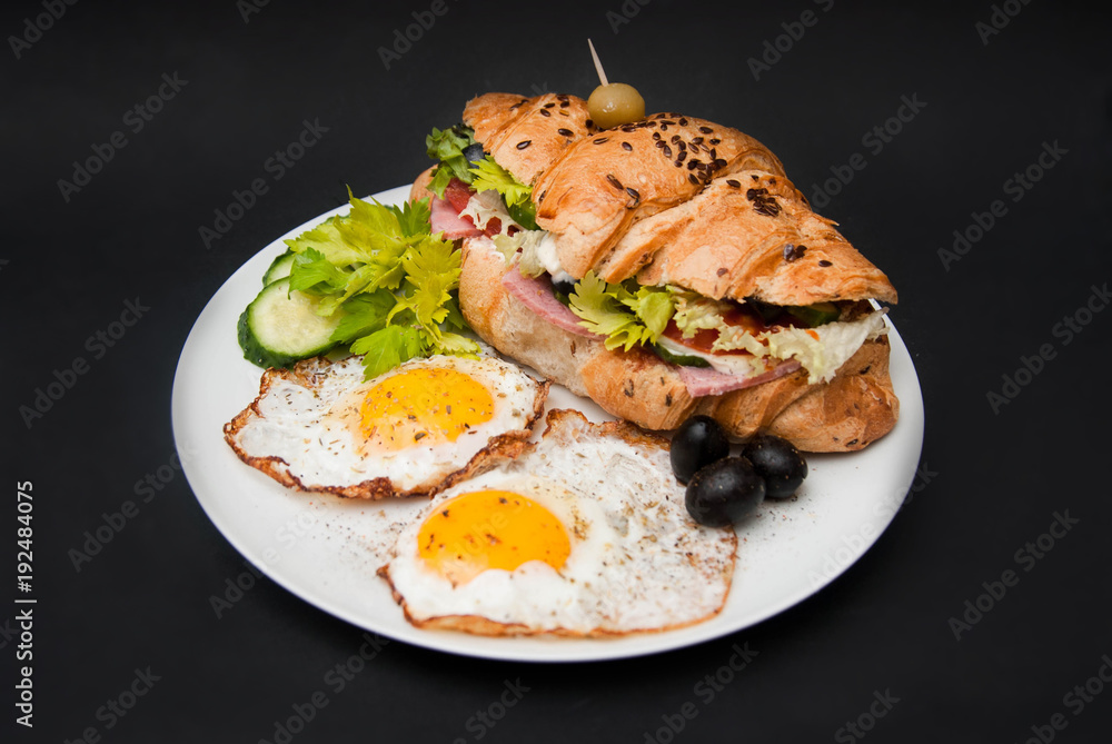 Fried Eggs with Croissant Sandwich and Fresh Vegetables over Black Background. Breakfast.