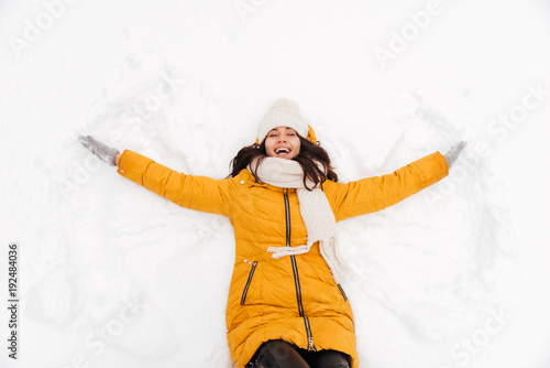 Happy playful lady lying on snow and making snow angel figure photo