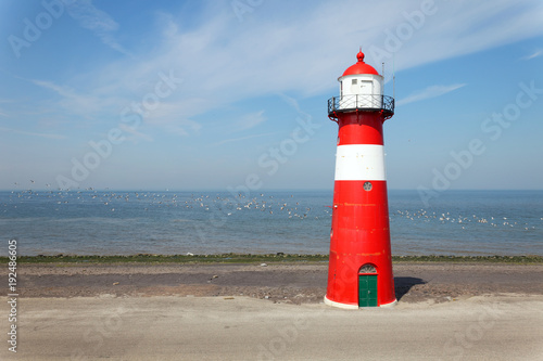 Red lighthouse on a dike seawall by the blue sea with seagull