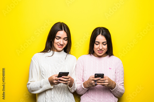 Photo of two cheerful girls chatting isolated over yellow background.