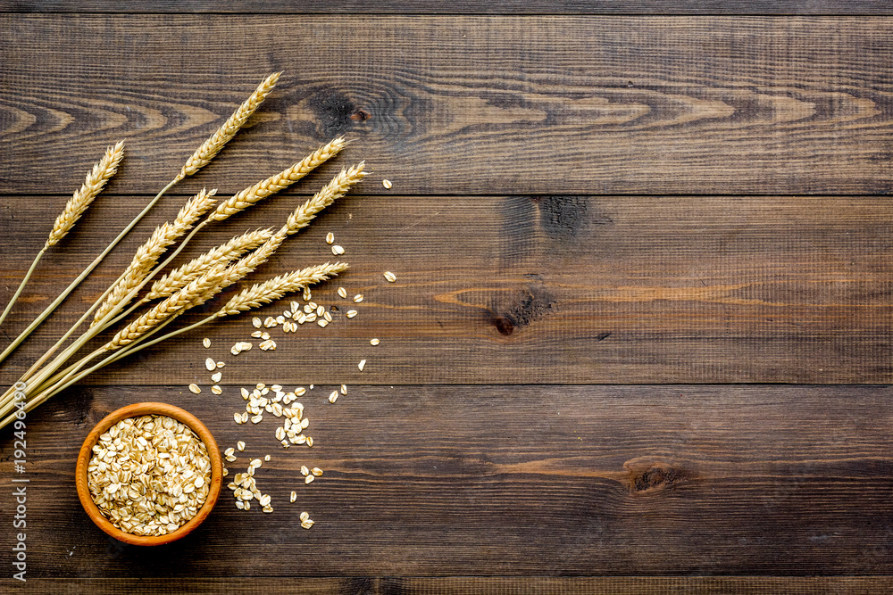 Cereals concept. Oatmeal in bowl near sprigs of wheat on dark wooden background top view copy space Cereals concept. Oatmeal in bowl near sprigs of wheat on dark wooden background top view copy space