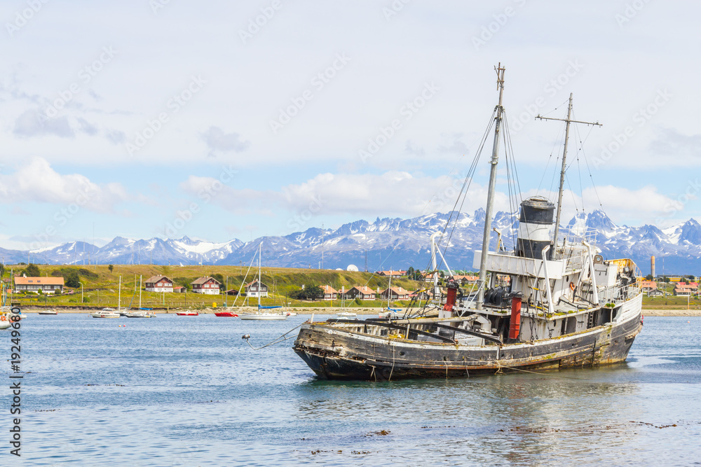 Old boat in Beagle channel with mountains and houses in Ushuaia