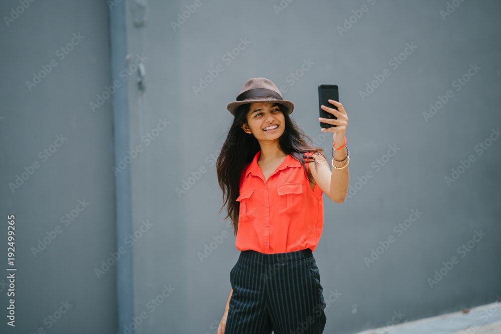 An image of a young and attractive Indian Asian woman taking a selfie while standing against a plain grey background. She is smiling and wearing a casual outfit for the day. An image of a young and attractive Indian Asian woman taking a selfie while standing against a plain grey background. She is smiling and wearing a casual outfit for the day.