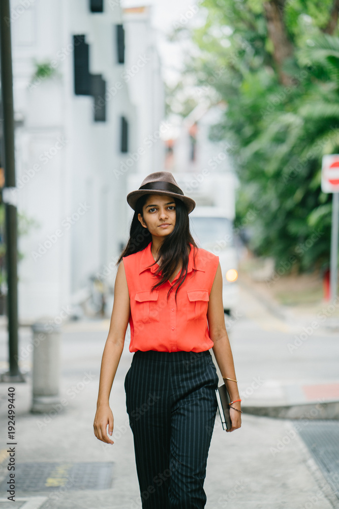 Portrait of a young and attractive  Indian Asian fashionista walking down the street in Singapore. She is dressed in a casual orange shirt and pants and smiling as she strides down the alley.