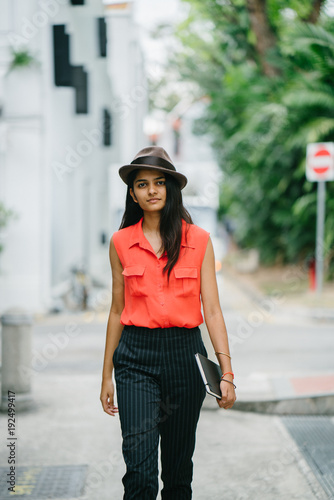 Portrait of an attractive young Indian Asian fashionist walking down Singapore's street. She is dressed in a casual orange shirt and pants, and as she steps down the alley, she smiles. © Danon