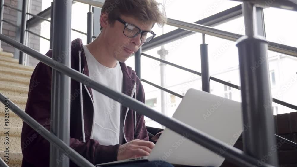 Young guy on the stairs with laptop, typing Young guy on the stairs with laptop, typing