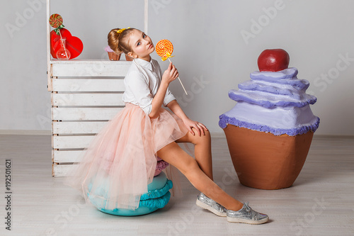 Beautiful teenage model girl in pink tutu or tulle skirts with colorful yellow lollipops in studio on white background  with artifitial big macaroons, fancy cakes and sweets photo