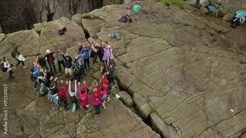 Aerial view from drone on breathtaking cliff called Preikestolen. Group of young people is standing on the cliff and making the heart and raising hands up with hands. 4k footage, upper view. Norway.