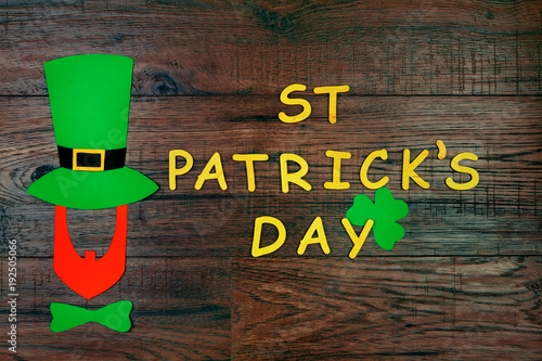 Saint Patrick's Day. Gold wooden letters "St Partick's Day" with silhouette of leprechaun in green hat and green tie bow with green three petal clover on wooden background