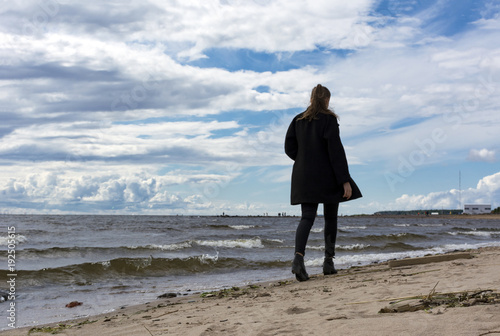 girl in black is on a sandy beach along the sea, the Gulf of Finland, cold water