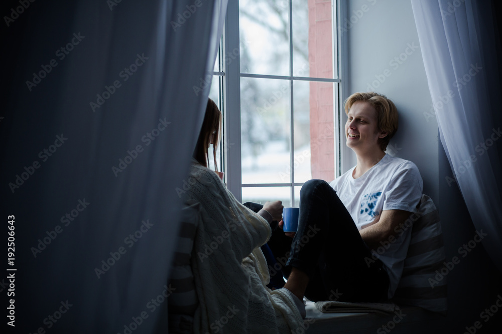 Cheerful pair of lovers spend time together. Sit on the window-sill and enjoy silence. Cheerful pair of lovers spend time together. Sit on the window-sill and enjoy silence.