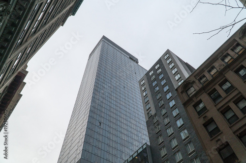 Look up vertical view of New York City style skyscraper office building and smaller apartments below from street level