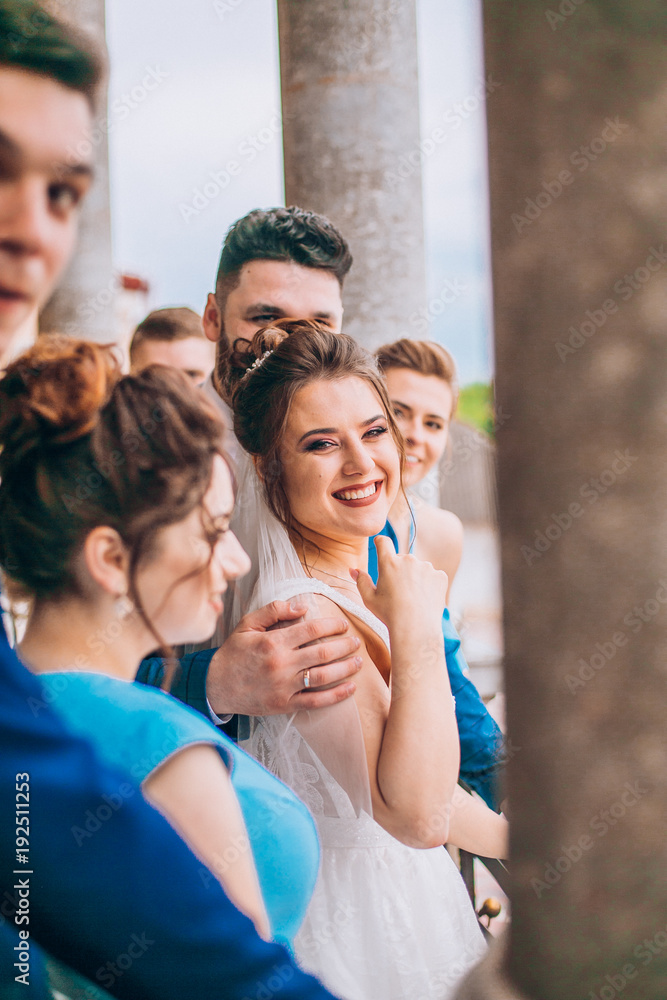 Full length portrait of newlywed couple and their friends at the wedding party. Bridesmaids and groomsman with Bride and groom near columns