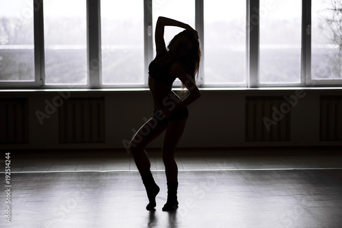 Silhouette of a sporty girl on a window background. Woman in the dance hall. The girl goes in for sports. Place and background for your text.