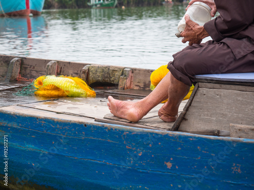 Vietnamese fisherman in traditional clothes closeup sitting in a wooden boat without a foot on the left leg