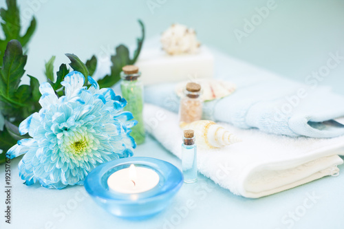 Aromatherapy spa concept with essential oil in blue glass bottle, sea salt, soap bar, candle, towel, flowers and sea shells on blue background, instagram