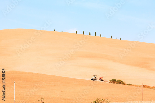 The tractor stands on a large  spacious hill with smooth lines in the Italian region of Tuscany amid a clear blue sky.