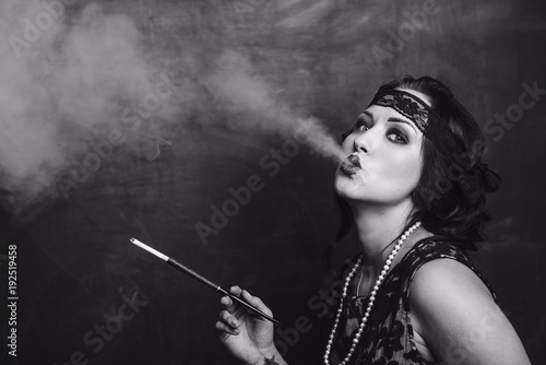 Fotografija brunette girl in black dress in the style of decadence holds the mouthpiece and