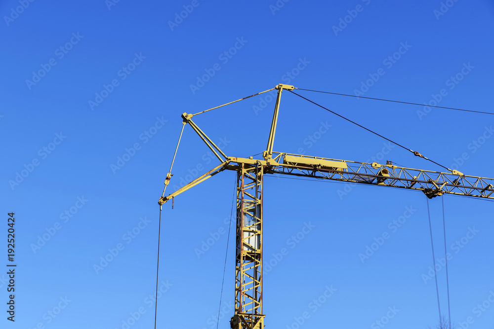 High construction crane of yellow color against the blue sky.