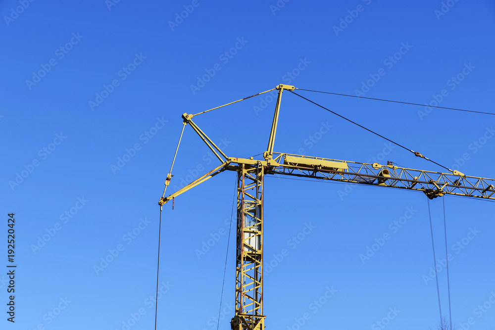 High construction crane of yellow color against the blue sky. High construction crane of yellow color against the blue sky.