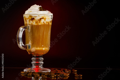 кофе латте со взбитыми сливками в высоком стеклянном стакане на черном фоне, а внизу рассыпаны зерна кофе 