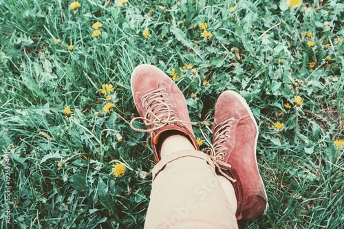 Female legs in sneakers on grass lawn with dandelions