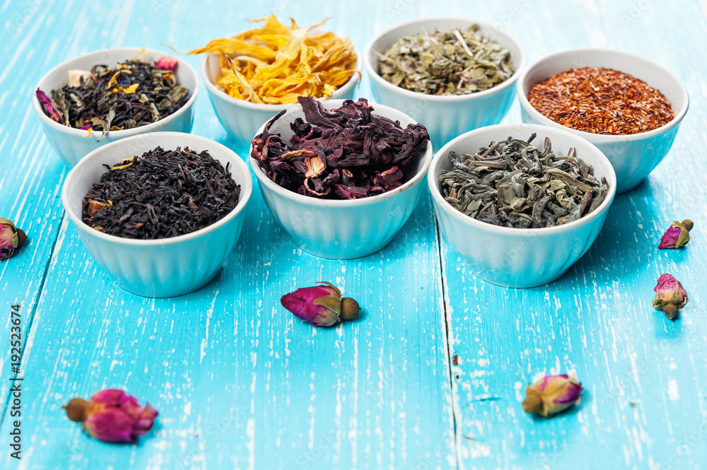 Various dried medicinal herbs and teas in several bowls on blue wooden background