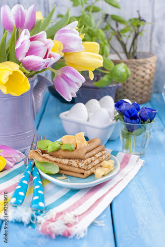 Homemade traditional pancakes with parmesan and basil for spring carnival. Italian breakfast. Bright flowers of tulips. Blue background. A free place for text or a postcard.