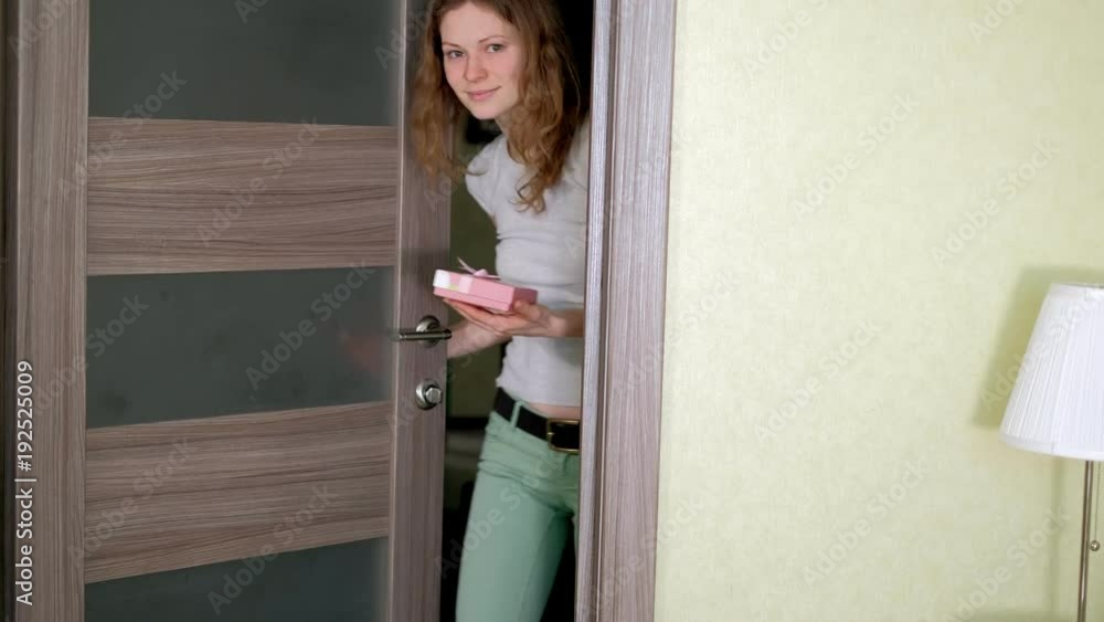 A woman enters the door and presents a gift in a box A woman enters the door and presents a gift in a box