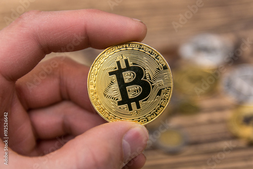  bitcoin holding in man’s fingers on old wooden background