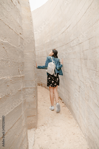 Attractive young woman stands between concrete walls. Caucasian girl in casual jeans looks up. © GotovyyStock