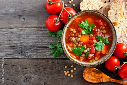 Homemade tomato, lentil soup, above view corner border with copy space on a rustic wood background