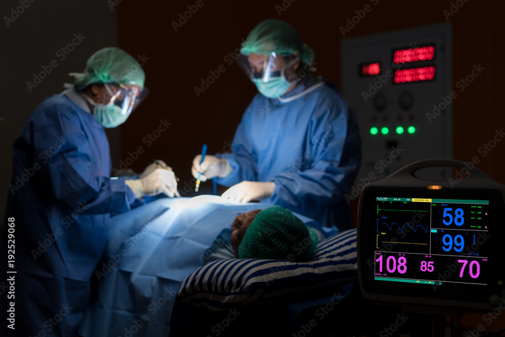 Electrocardiogram in hospital surgery operating emergency room showing patient heart rate with blur team of surgeons in background. Health and medicine concept.. Electrocardiogram in hospital surgery operating emergency room showing patient heart rate with blur team of surgeons in background. Health and medicine concept..