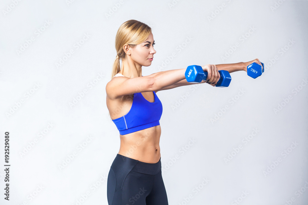 Profile view of blonde woman, showing two blue dumbbells. Profile view of blonde woman, showing two blue dumbbells.