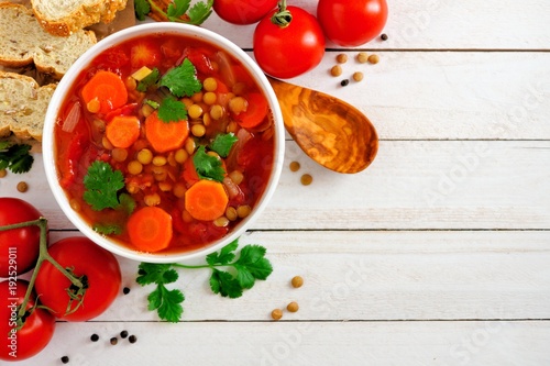 Homemade tomato, lentil soup, above view corner border with copy space on a white wood background