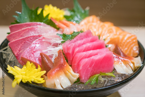 Mixed sliced fish sashimi on ice in black bowl. Sashimi Salmon Tuna Hamachi Prawn and Surf Calm set, raw fish, japanese food in Asian restuarant.